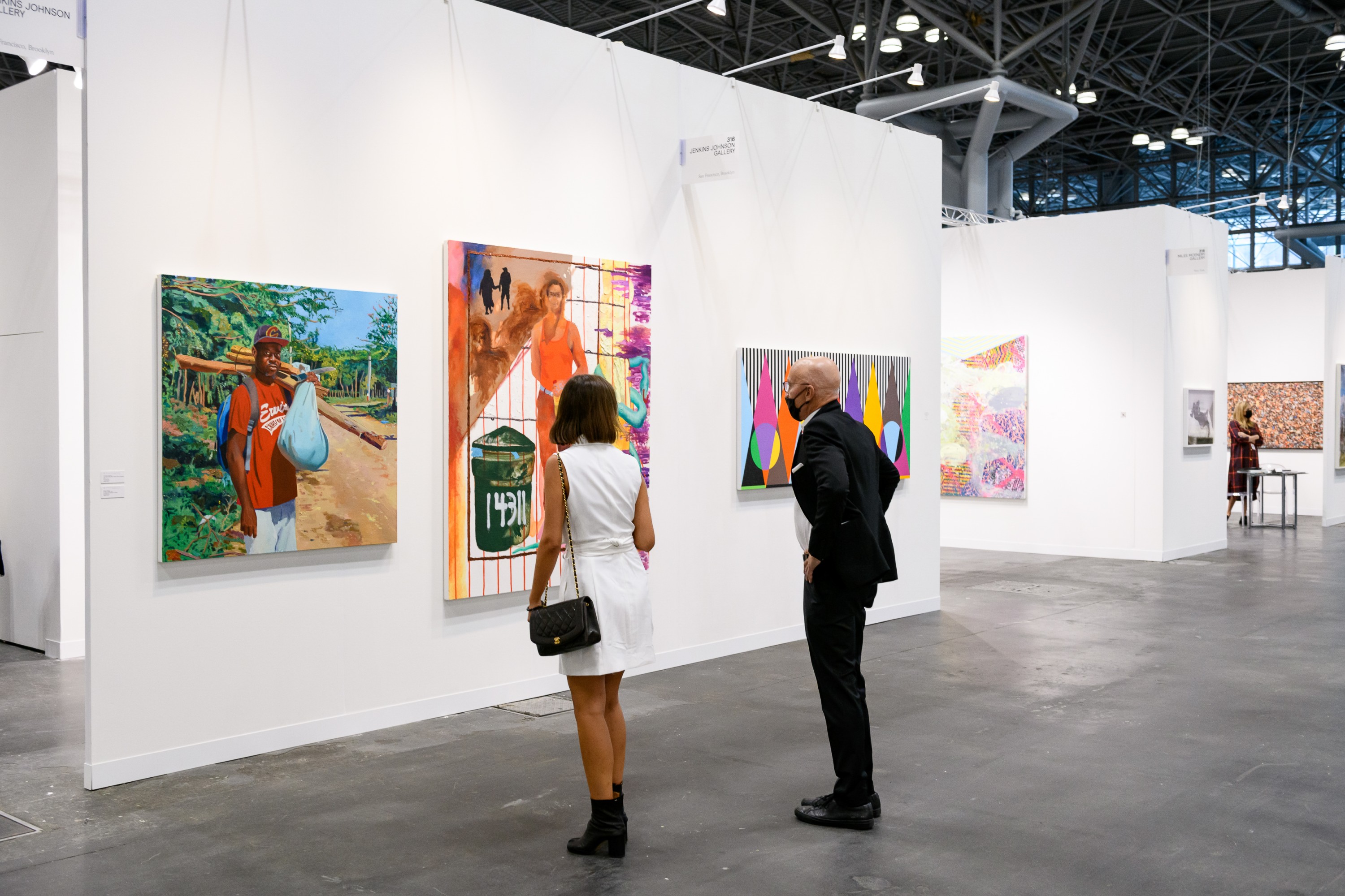 A man and a woman visiting The Armory Show, New York's Art Fair at the Javits Center, looking at two contemporary paintings.